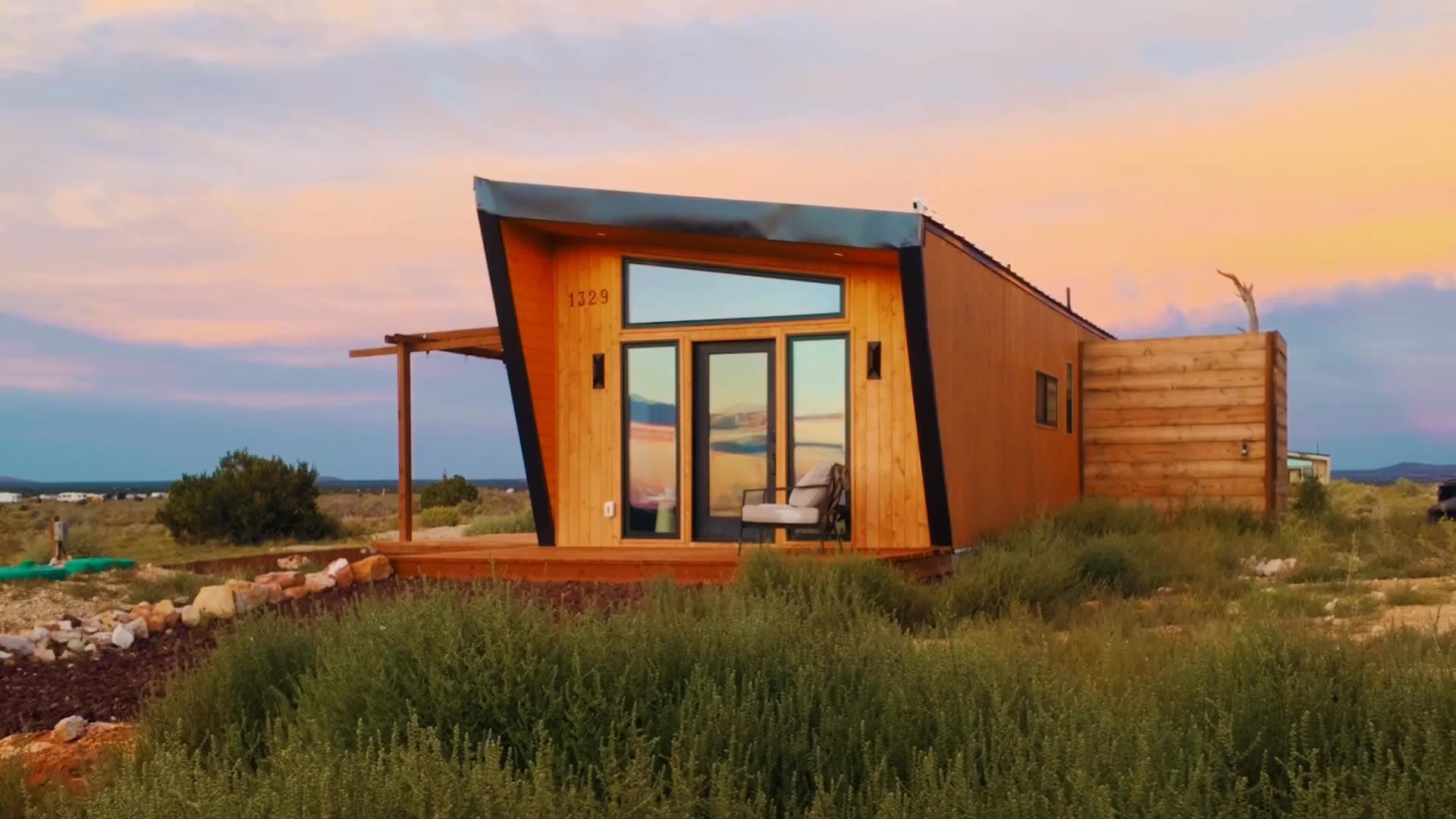 Venus, a wood-clad Stargazing tiny home with glass doors and a deck, in the desert at sunset